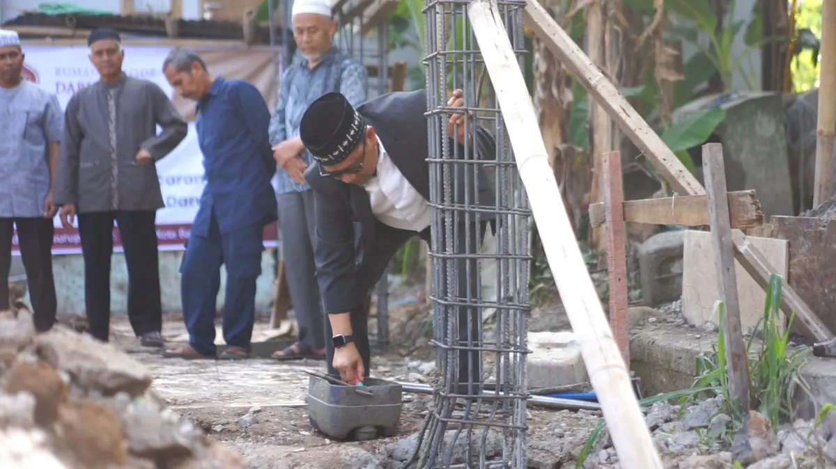 Beberapa orang berjongkok dan berdiri di sekitar bekisting dan rangka besi kolom saat proses pengecoran